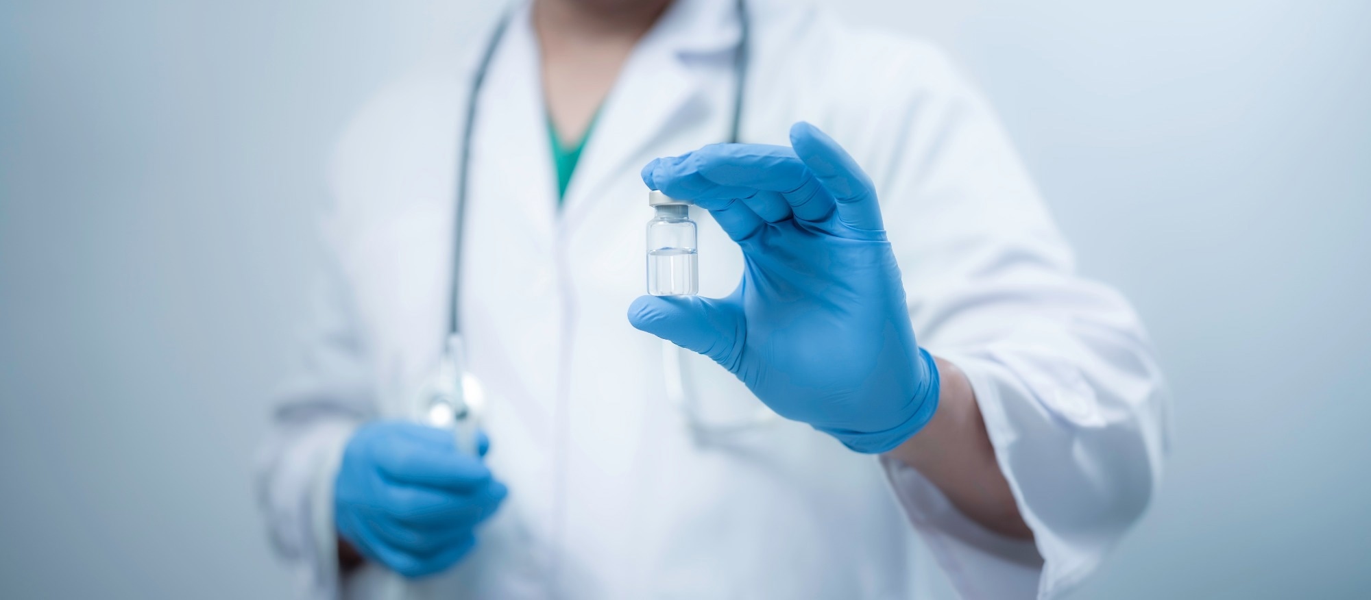 A medical worker wearing a white coat is holding a vaccine bottle.