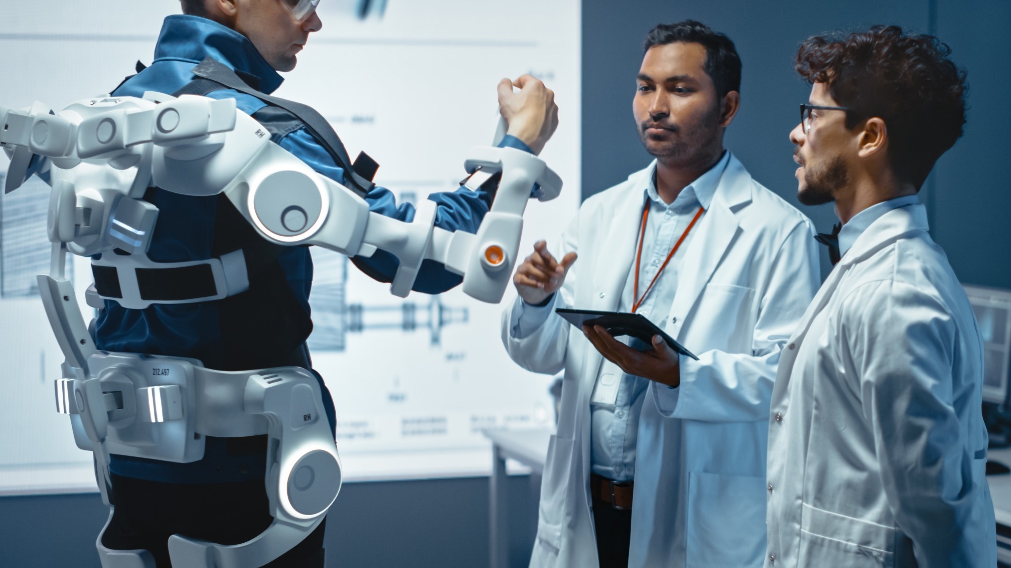 In Robotics Development Laboratory: Engineers and Scientists Work on a Bionics Exoskeleton Prototype with Person Testing it. Designing Wearable Exosuit to Help Disabled People.