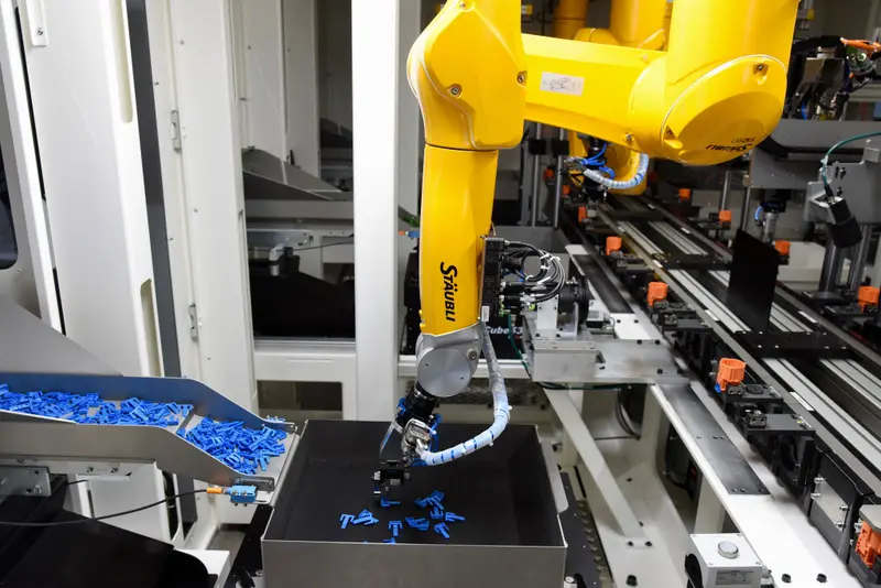 The second Stäubli six-axis robot picks up a connector lock from a vibration platform and attaches it to the connector housing