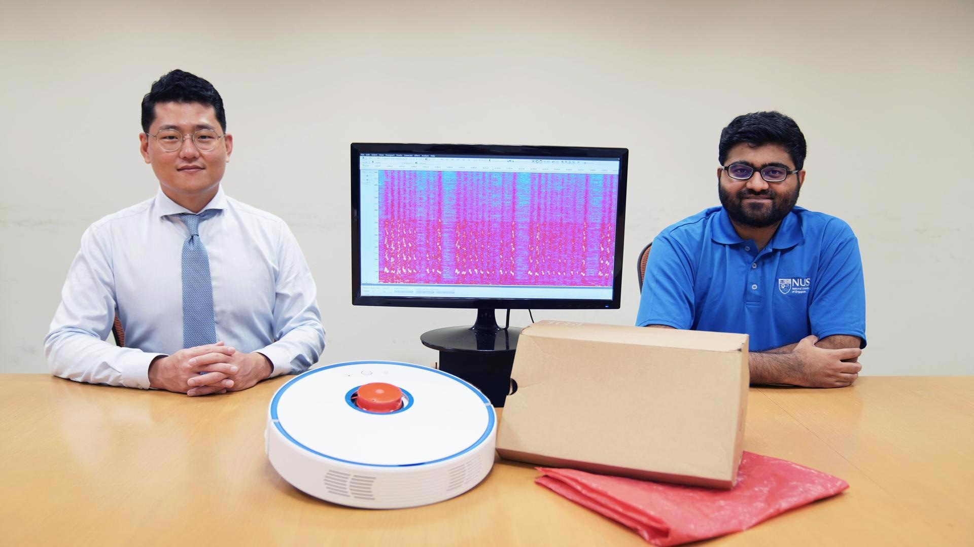 Assistant Professor Jun Han (left) and doctoral student Mr Sriram Sami (right) from NUS Computing with a robot vacuum cleaner, a monitor showing recovered sound waves, and common household items made from materials that can reflect sound. Image Credit: National University of Singapore.