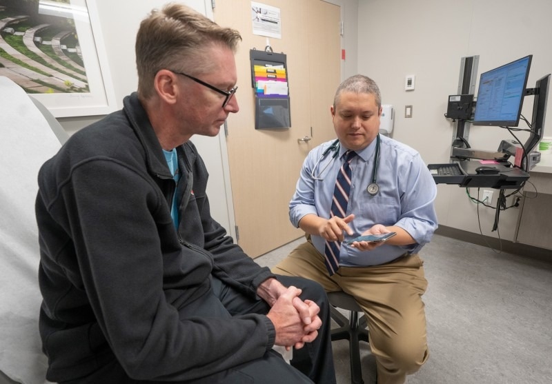 Dr. Harrison Jackson explains the use of AI-powered ambient documentation to his patient. This application listens and drafts notes from the appointment so the physician does not need to.