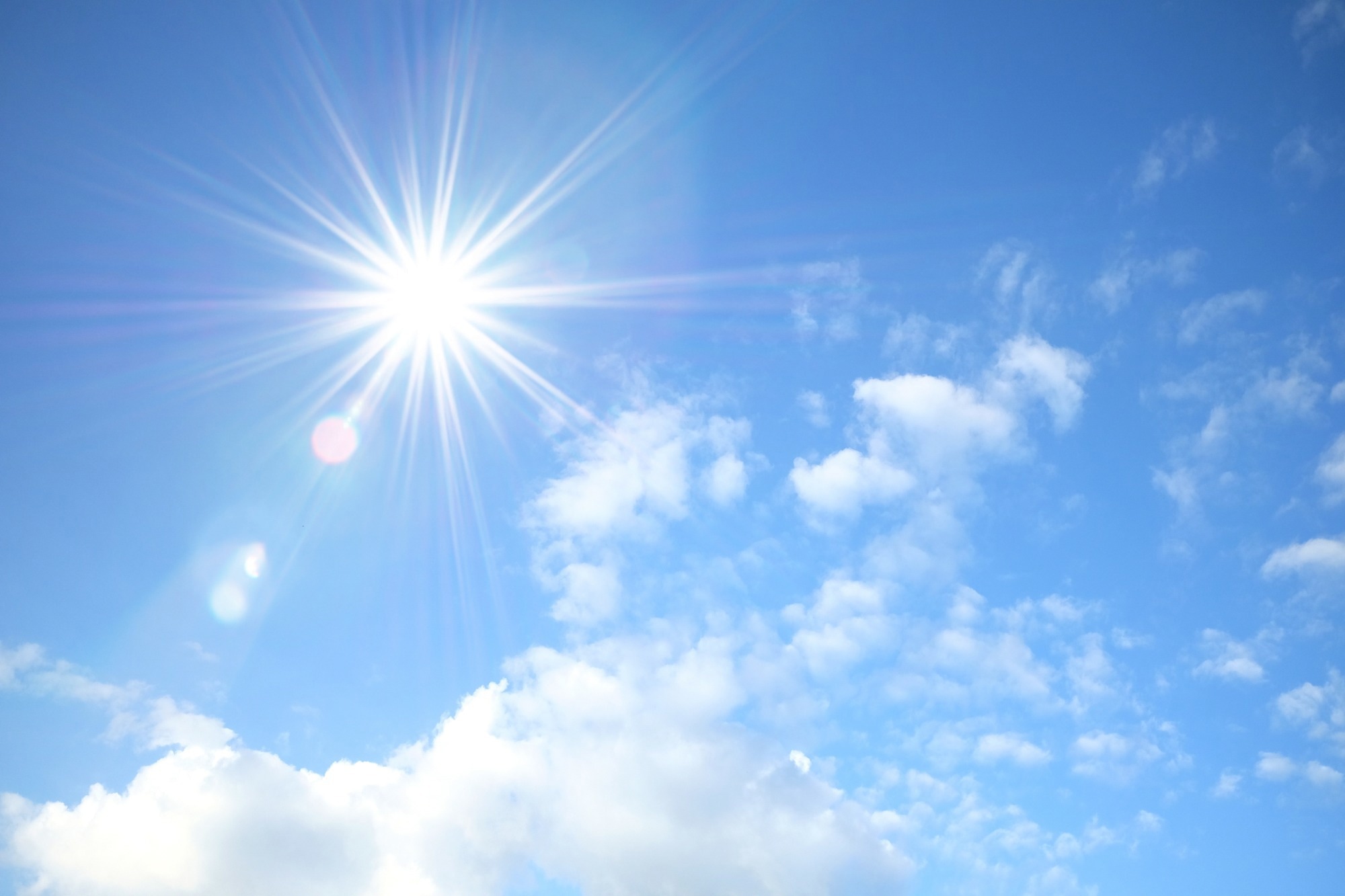 Blue sky with white fluffy clouds and sun reflection.