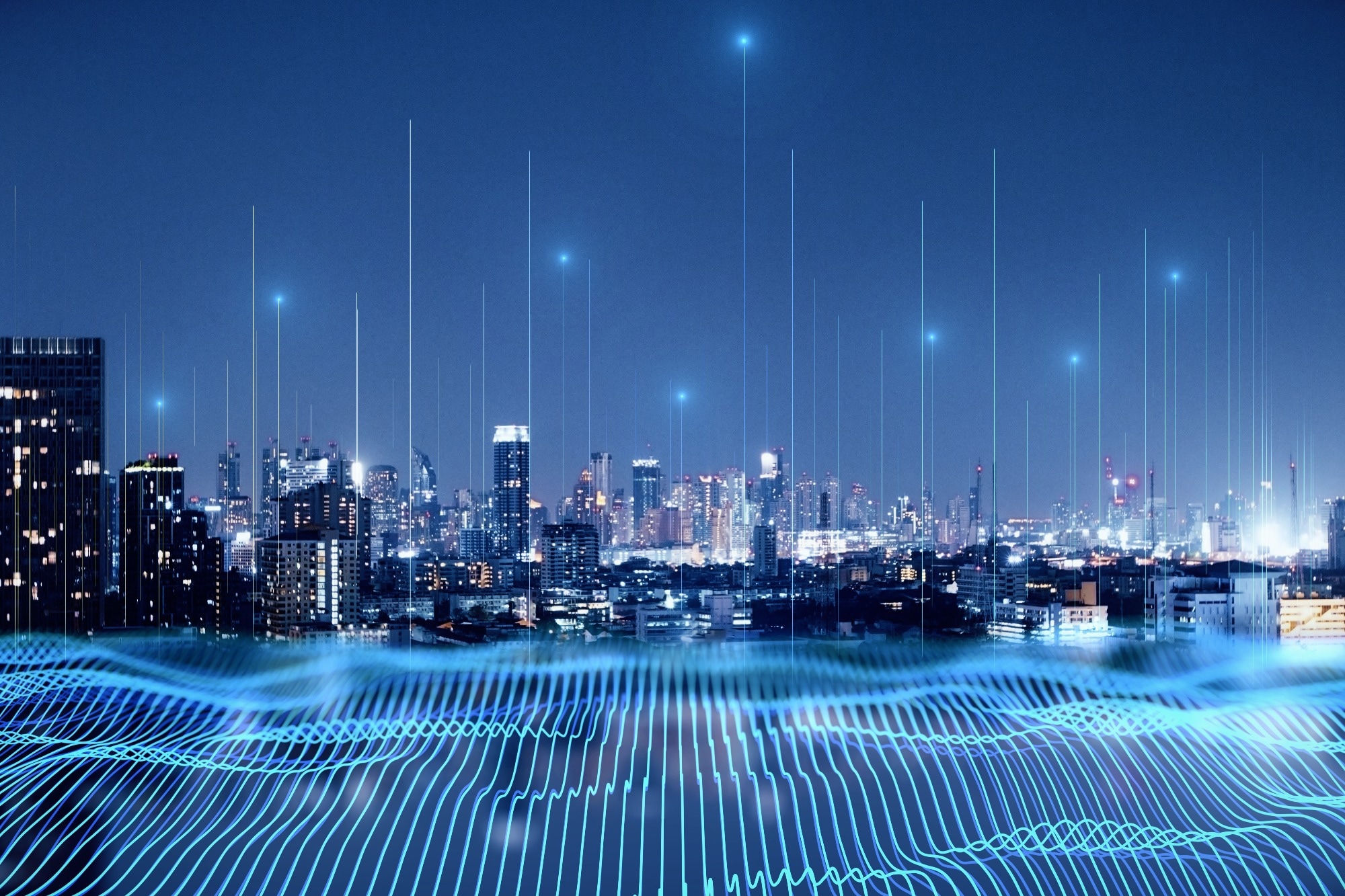 Smart city and big data connection technology concept with digital blue wavy wires with antennas on night megapolis city skyline background, double exposure