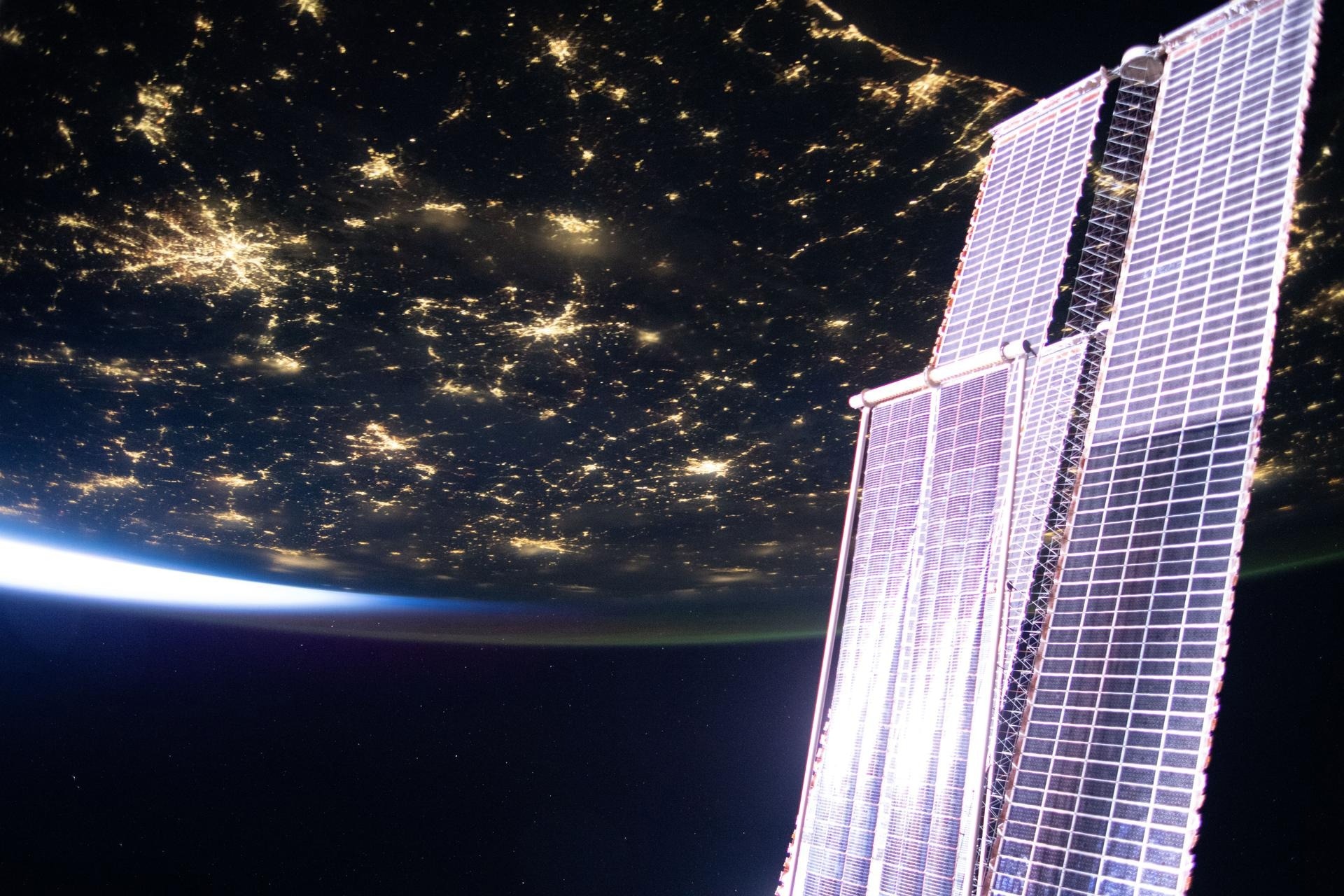 In the right foreground, part of the station’s main solar arrays is visible, alongside a smaller set of roll-out solar arrays that help power the orbital outpost.