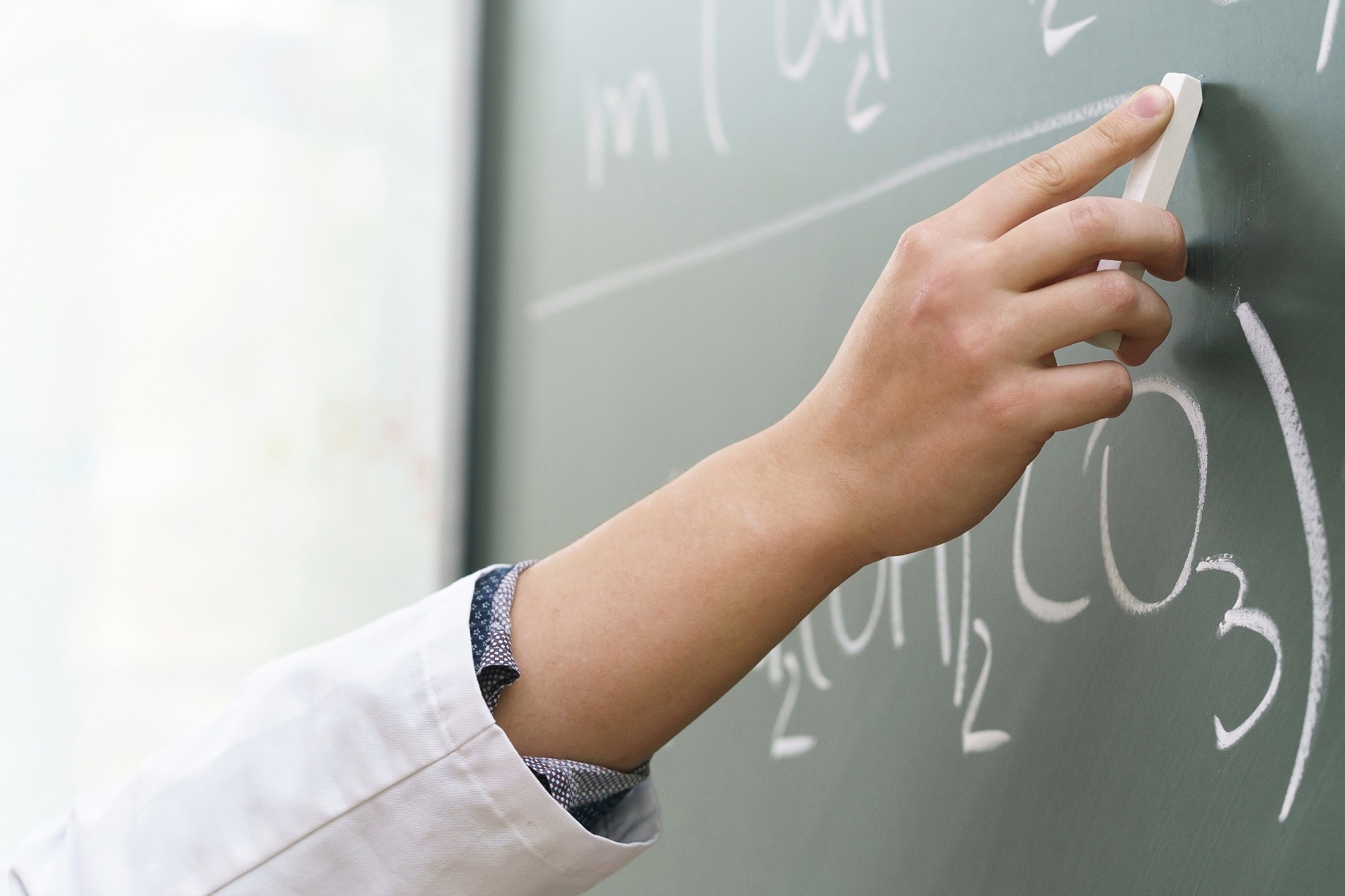 Closeup of scientist hand with a chalk writing a chemical equation.