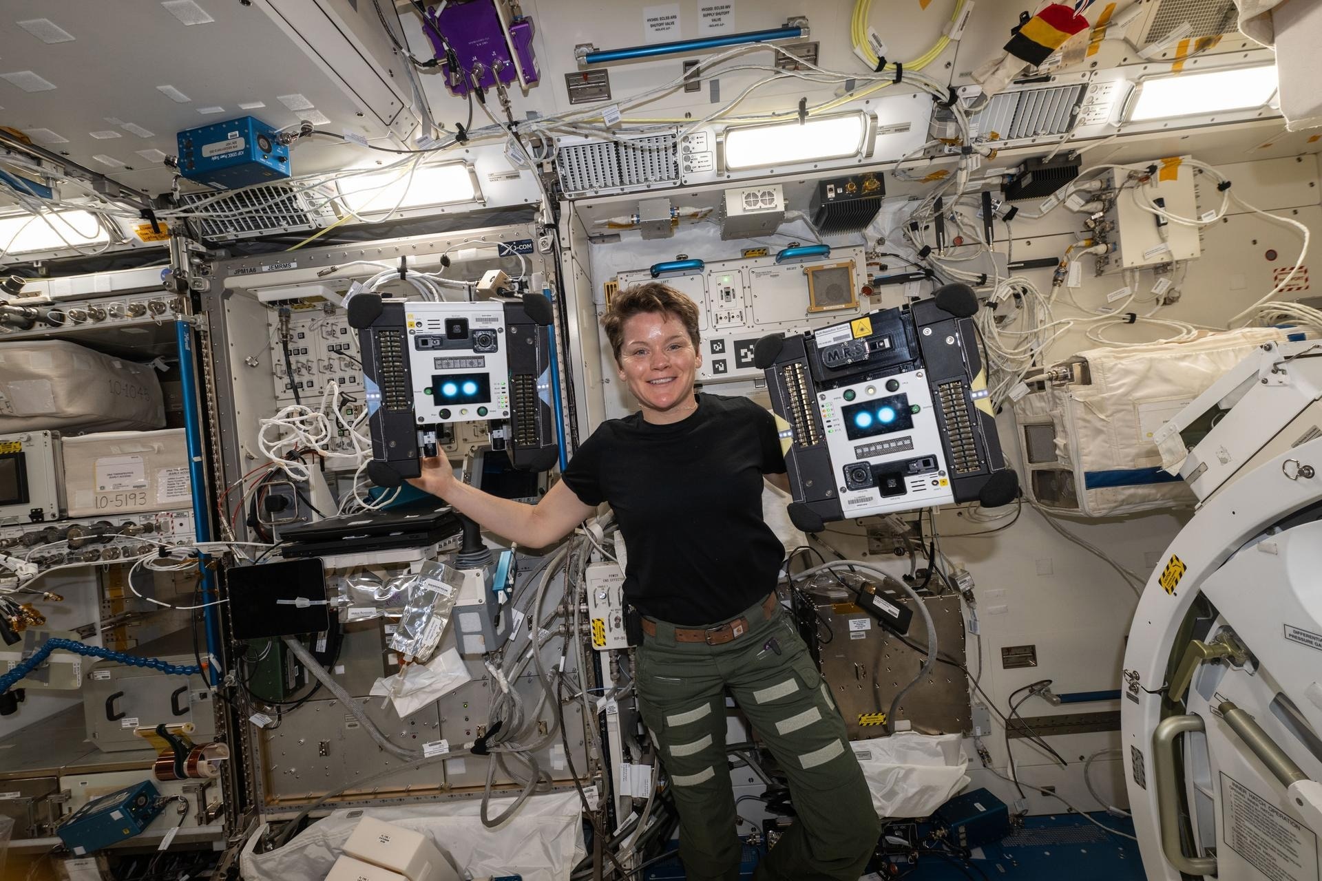 NASA astronaut McClain poses with Astrobee robots Bumble (left) and Honey during their latest on orbit activity in May, 2025.