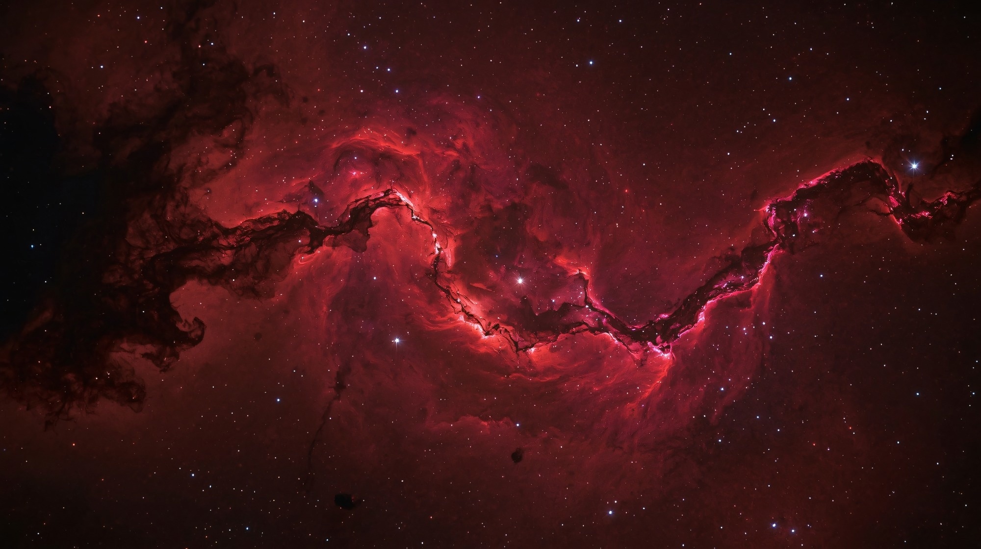 A stunning red nebula stretching across deep space, filled with glowing gas, dark dust clouds, and bright stars scattered throughout the cosmic background.